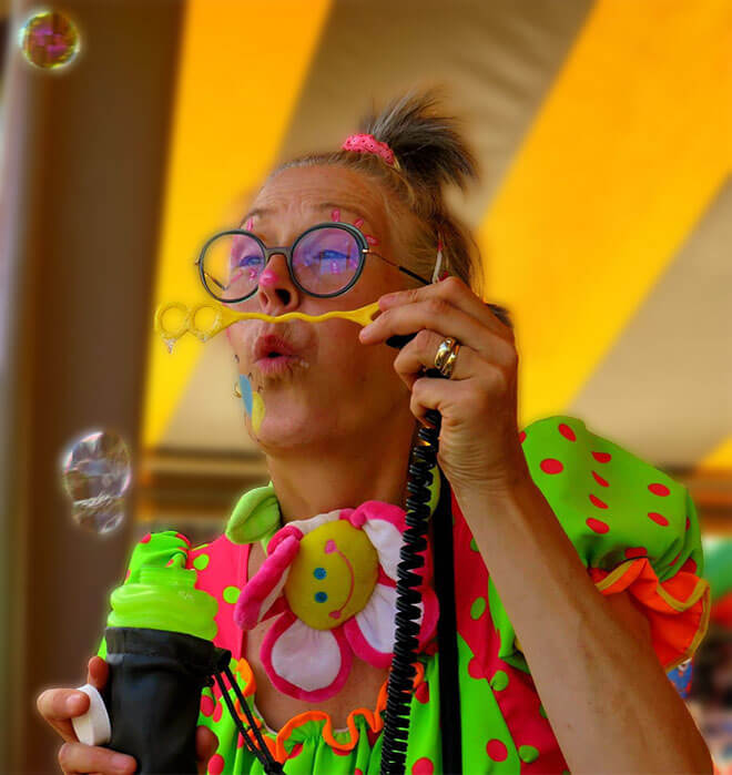 Female cliniclowns blowing into a bubble toy during a performance for children